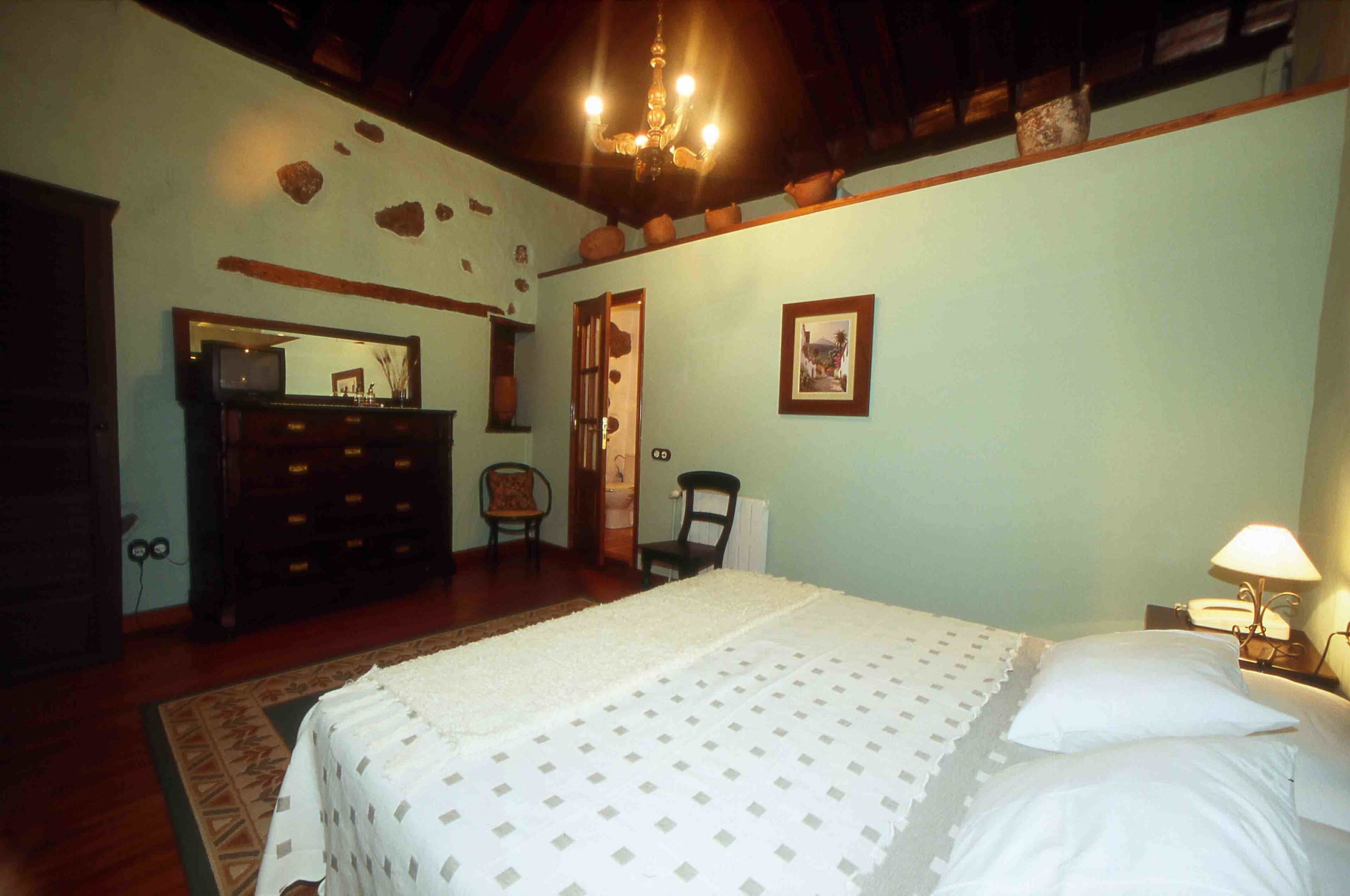 A bedroom with a bed, dresser, chair, and a lamp.
