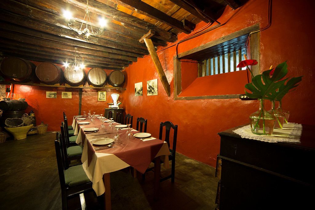 A dining area with a long table set for a meal, wooden chairs, and a rustic ambiance with exposed beams and wooden barrels on the wall.