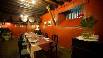 Un comedor con una mesa larga dispuesta para una comida, sillas de madera y un ambiente rústico con vigas a la vista y barriles de madera en la pared.
