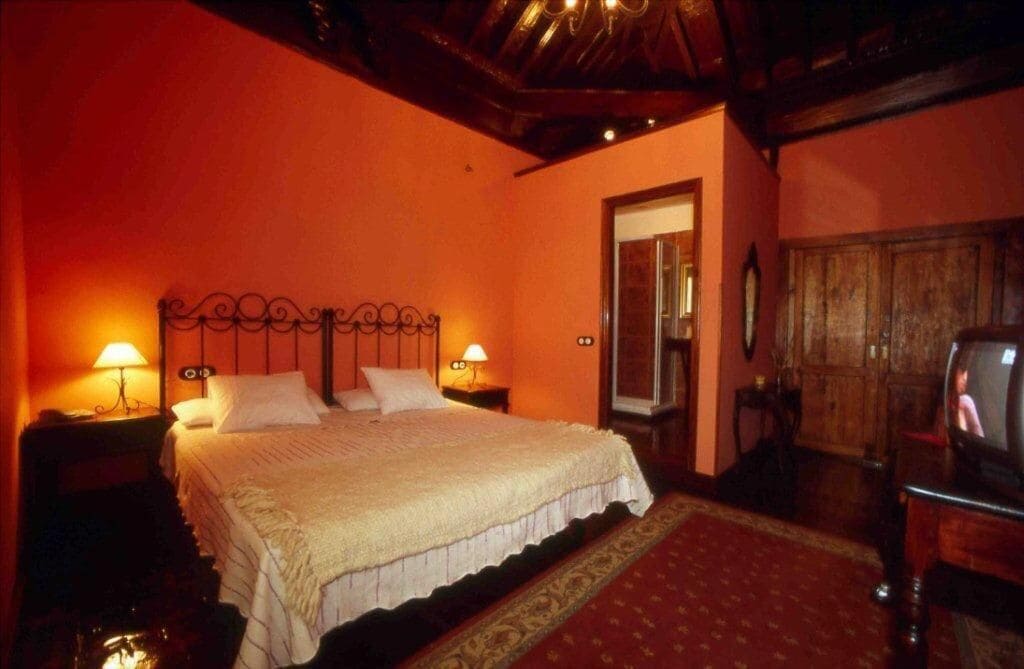 A bedroom with a large bed, two bedside lamps, a wooden wardrobe, and a television.