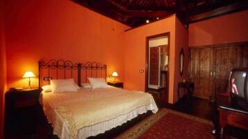 A bedroom with a large bed, two bedside lamps, a wooden wardrobe, and a television.
