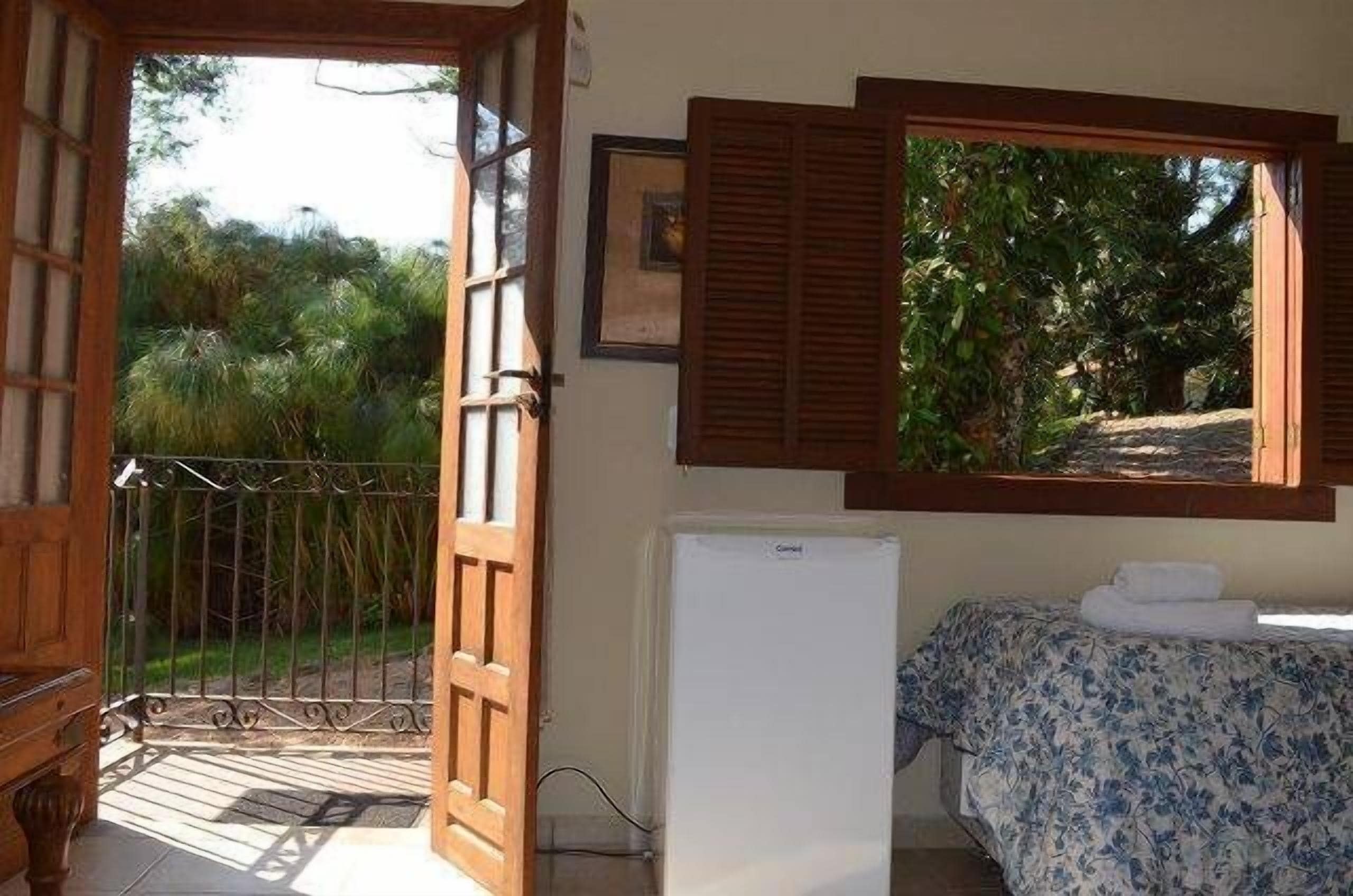 Una habitación con una cama, un refrigerador blanco, una puerta de madera y una ventana con contraventanas.