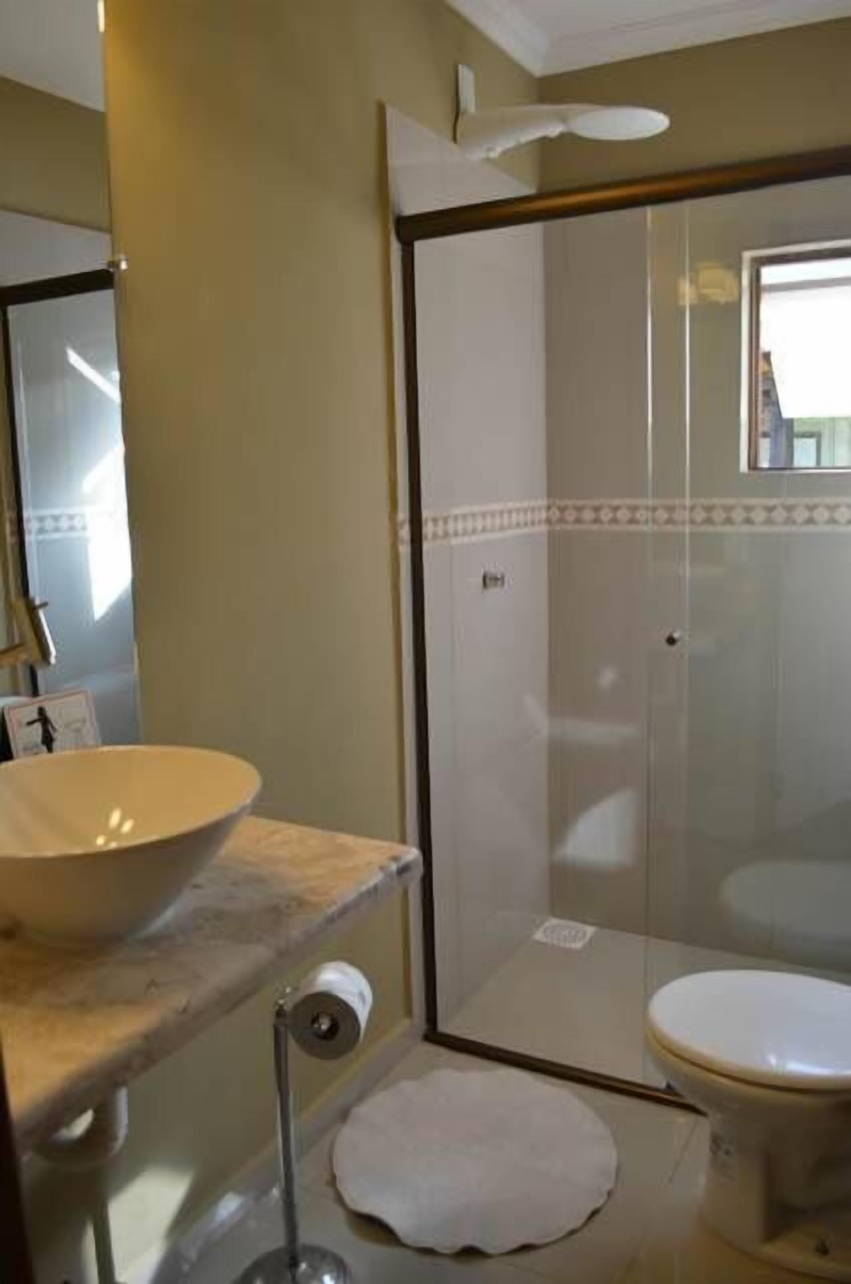 A bathroom with a large white sink, a toilet, and a glass shower enclosure.