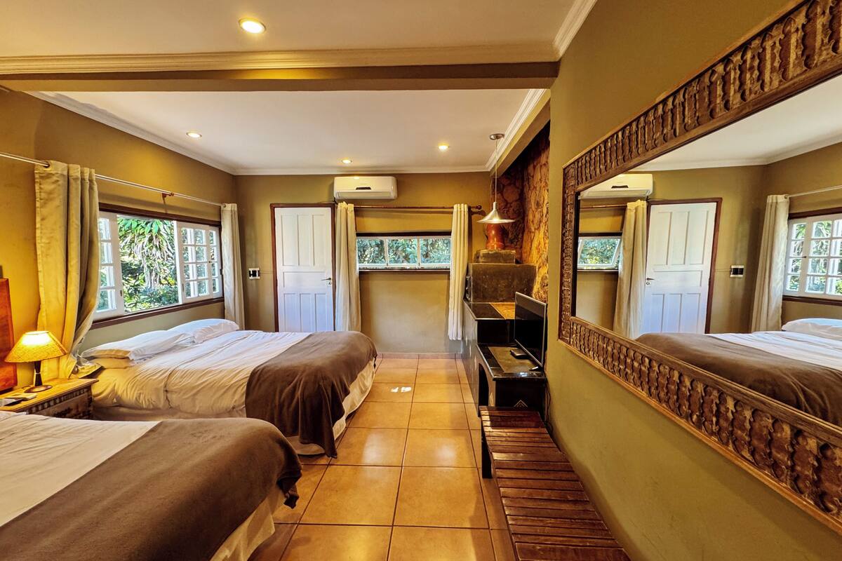Una habitación de hotel con dos camas, un escritorio pequeño, un espejo y una ventana con cortinas.