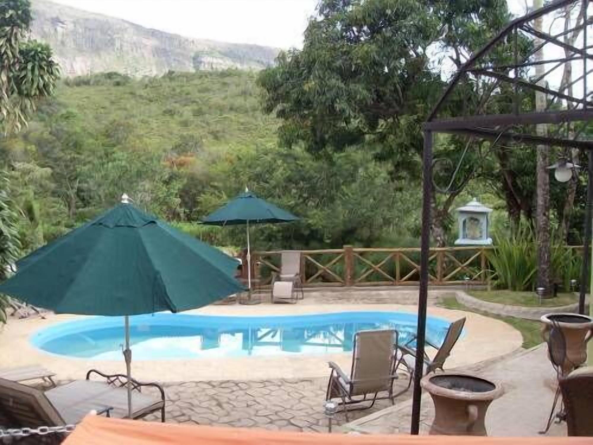 Un espace piscine agrémenté de chaises longues et de parasols, entouré d’une végétation luxuriante et dominé par un paysage montagneux.