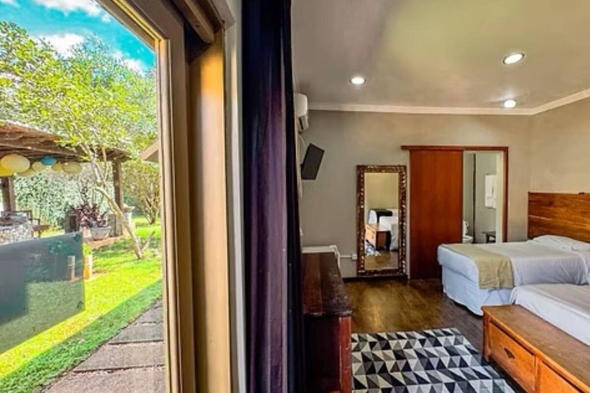 Habitación de hotel con dos camas, un espejo grande, un cabecero de madera y vistas al jardín.