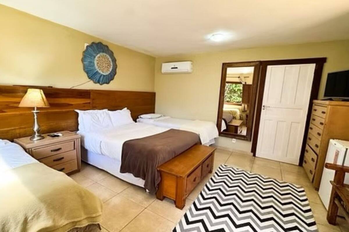 Habitación de hotel con cama, mesitas de noche, un banco, espejo, armario y televisión.