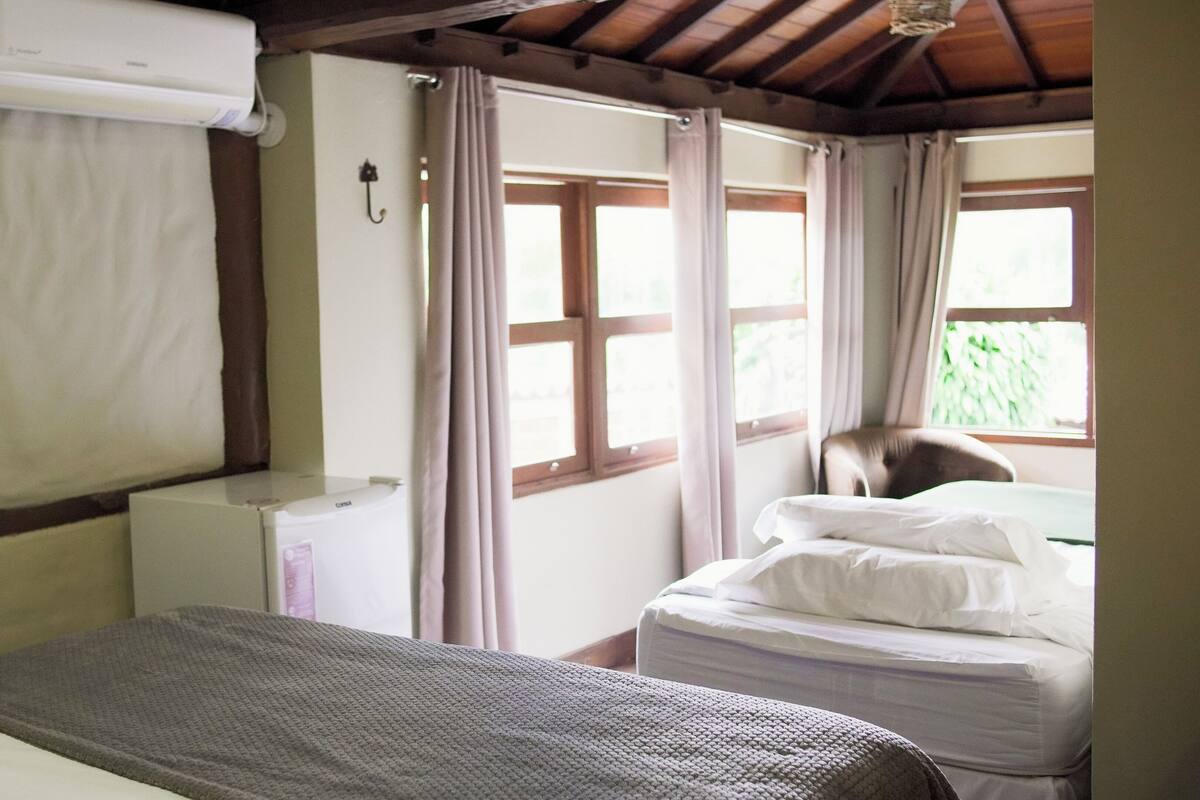 Una habitación con cama, ventana con cortinas y aire acondicionado de pared.