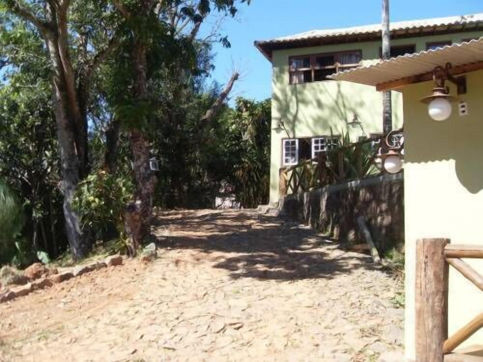 Un chemin de terre mène à une maison dont le toit est fait de tôles ondulées et qui est entourée d’une clôture en bois.