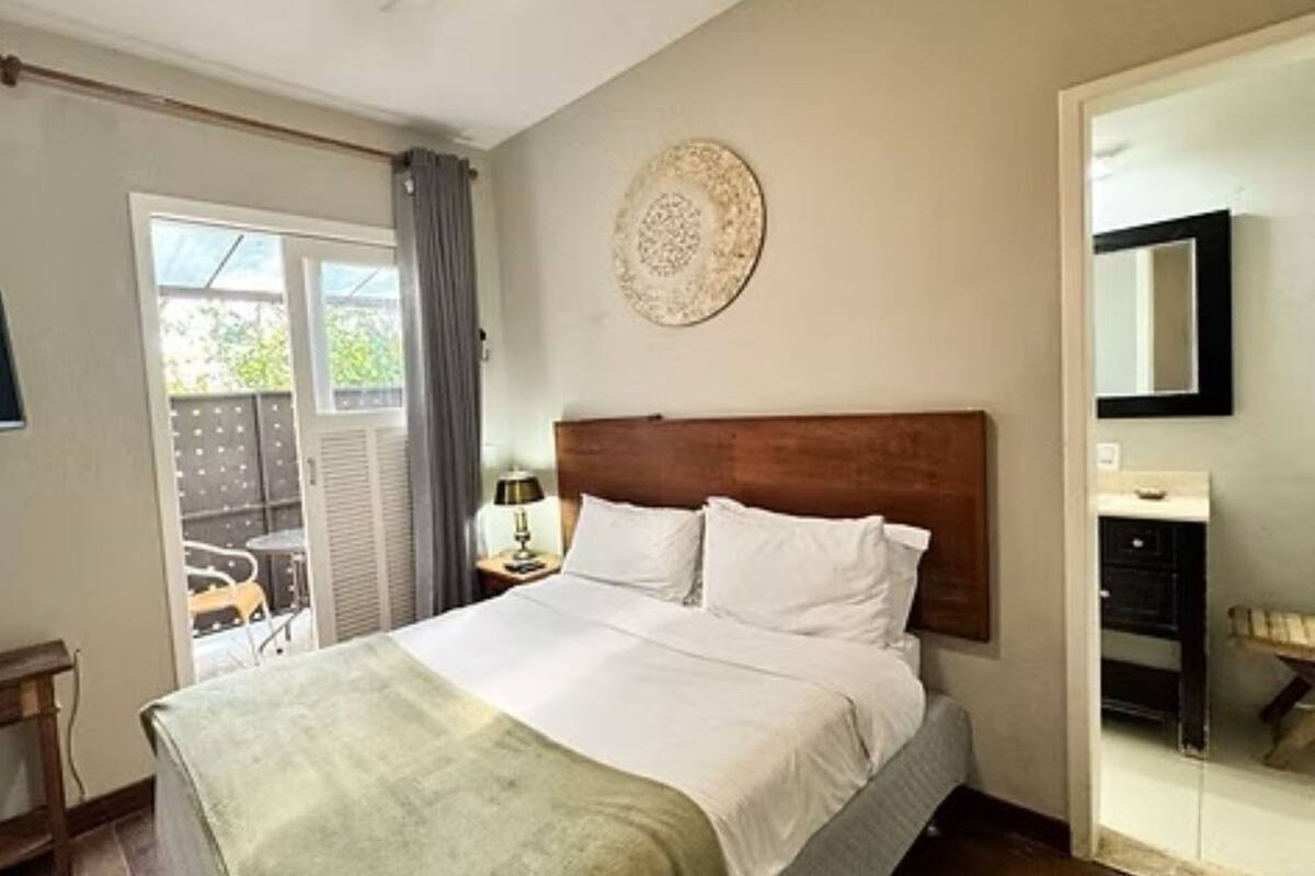 Un dormitorio con cama, televisión, una mesita, una silla y una puerta que da a un espacio exterior.