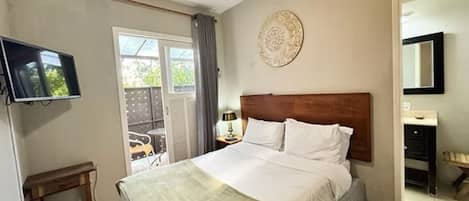 A bedroom with a bed, a television, a small table, a chair, and a door leading to an outdoor area.