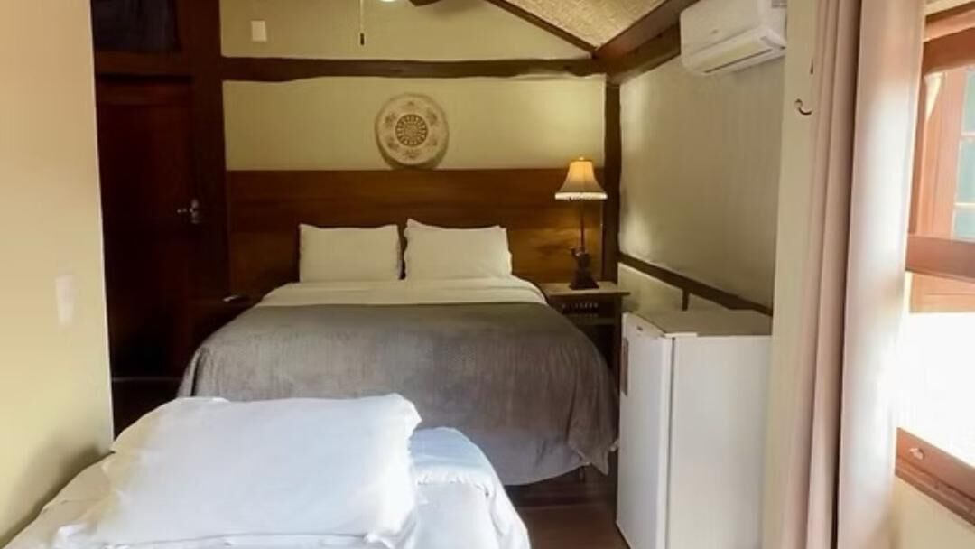 Een slaapkamer met een bed, nachtkastje, lamp en een klein kastje.