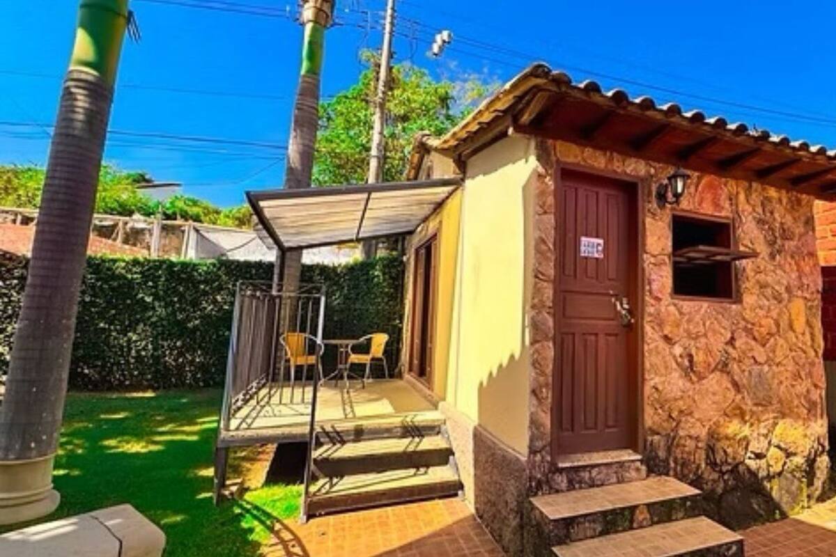 Un pequeño edificio de piedra con una puerta marrón, un porche cubierto con sillas y una ventana pequeña.