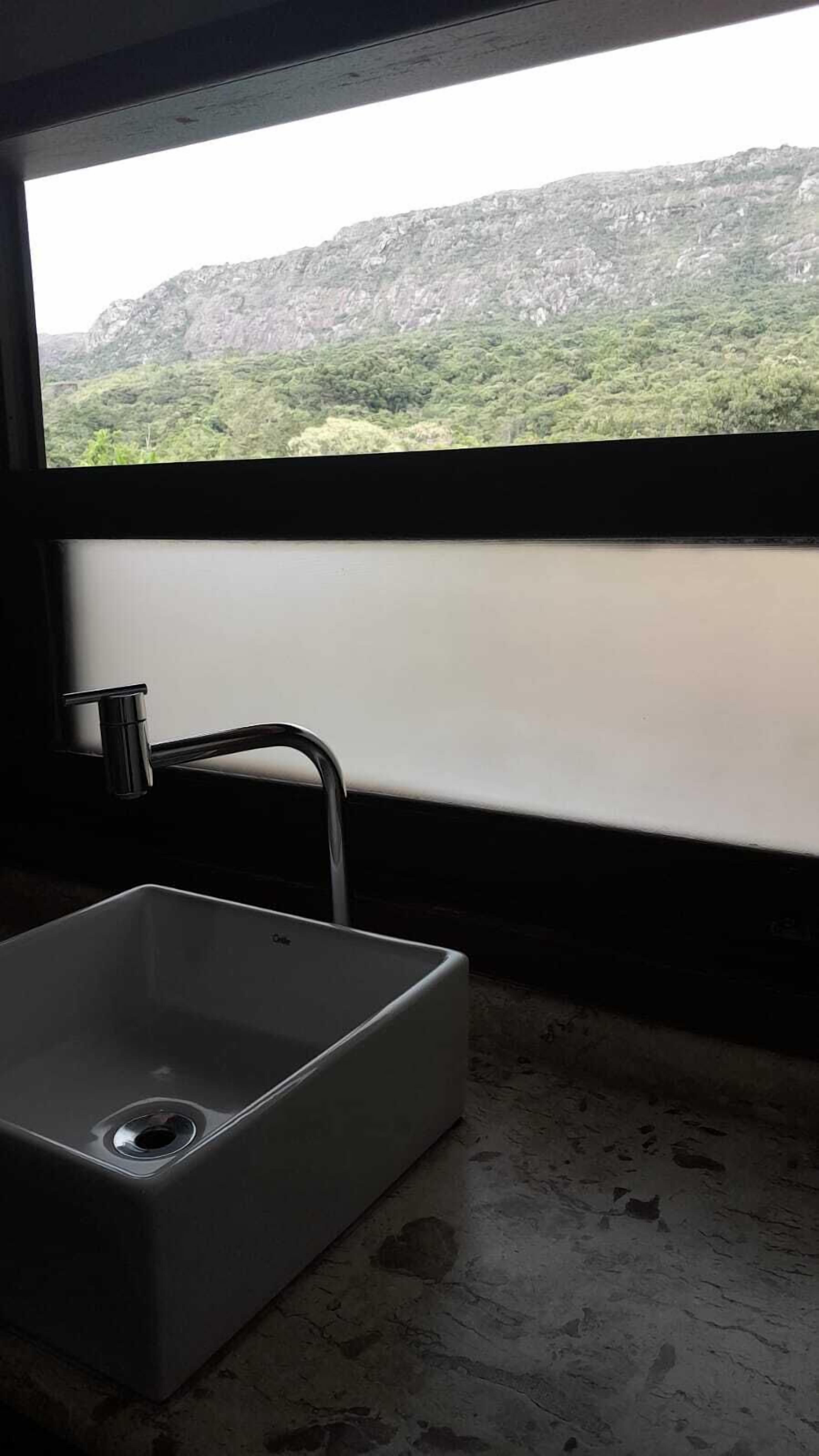 Ein Badezimmer mit Waschbecken, Wasserhahn und Fenster mit Blick auf eine Berglandschaft.