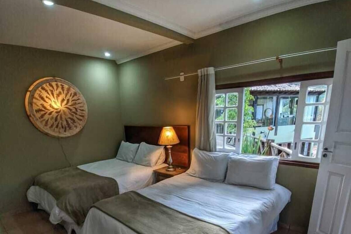 Una habitación con dos camas, una lámpara en la pared, un ventanal y una puerta.