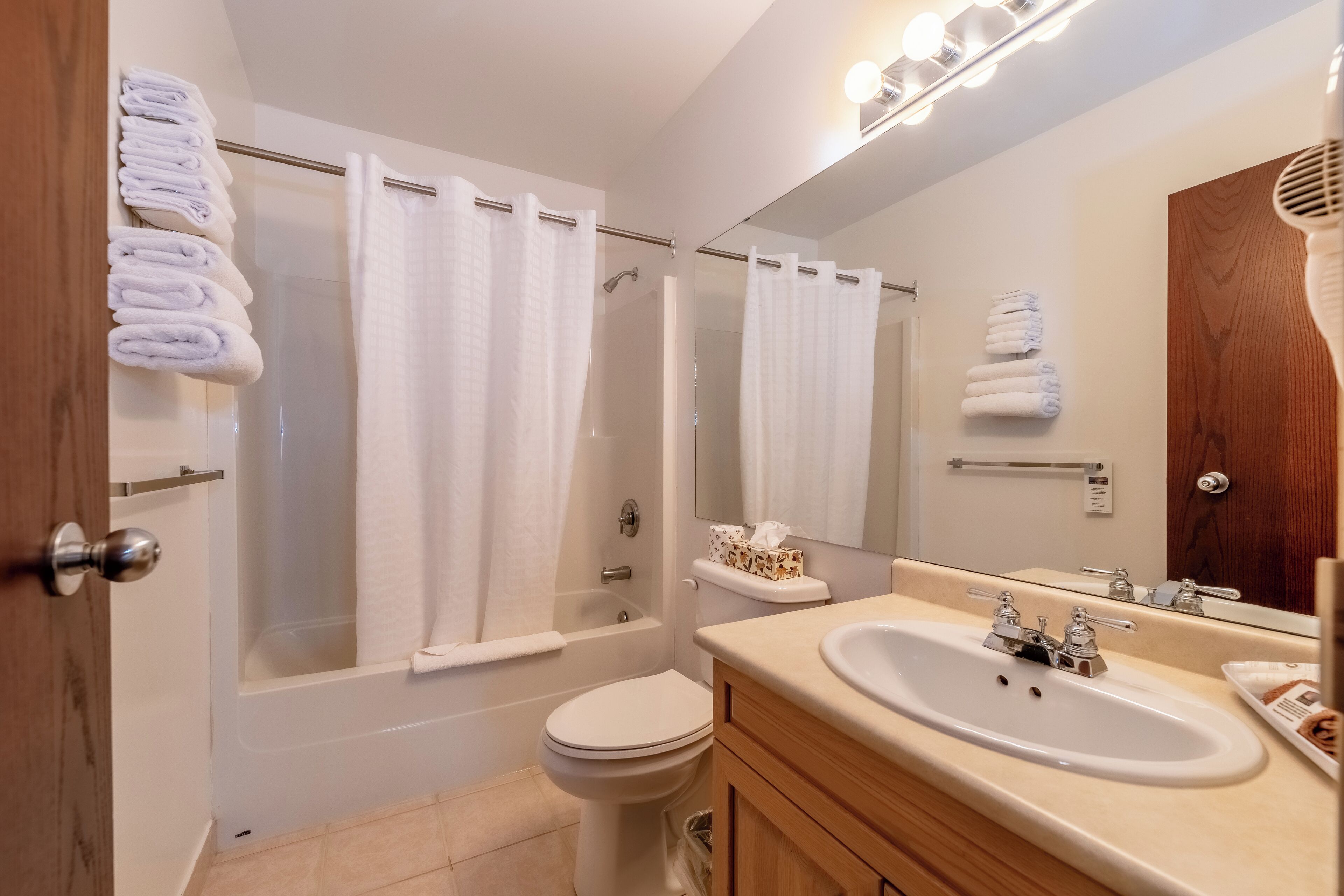 A modern bathroom with a bathtub, toilet, sink, and a mirror with lights.