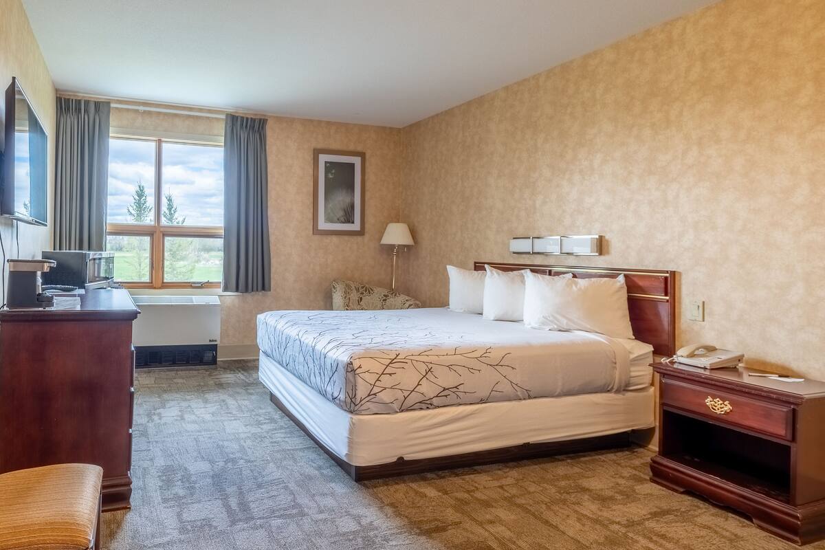 A hotel room with a large bed, a desk, a lamp, and a window with curtains.