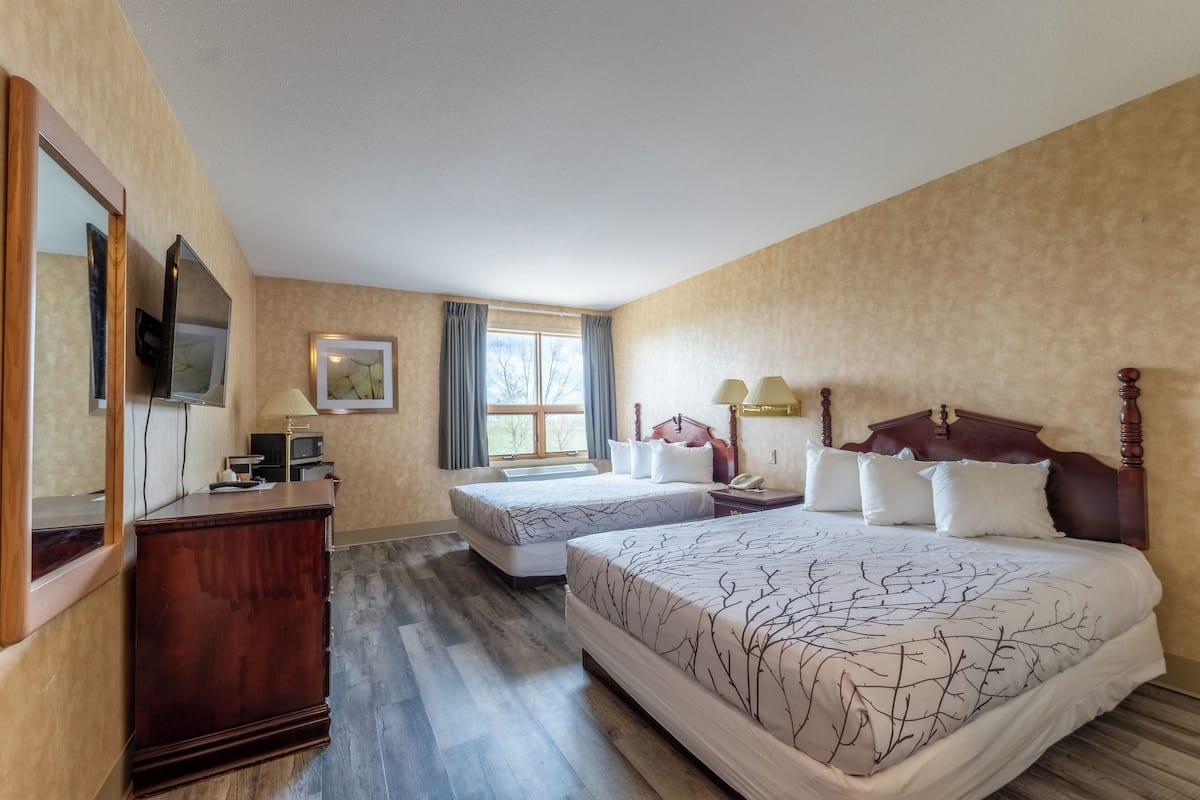A hotel room with two beds, a wooden dresser, a television, and a window with curtains.