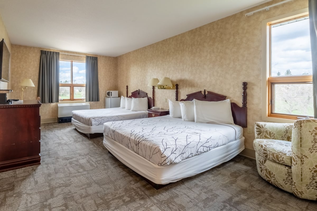 A hotel room with two beds, a wooden dresser, a chair, and a large window with curtains.