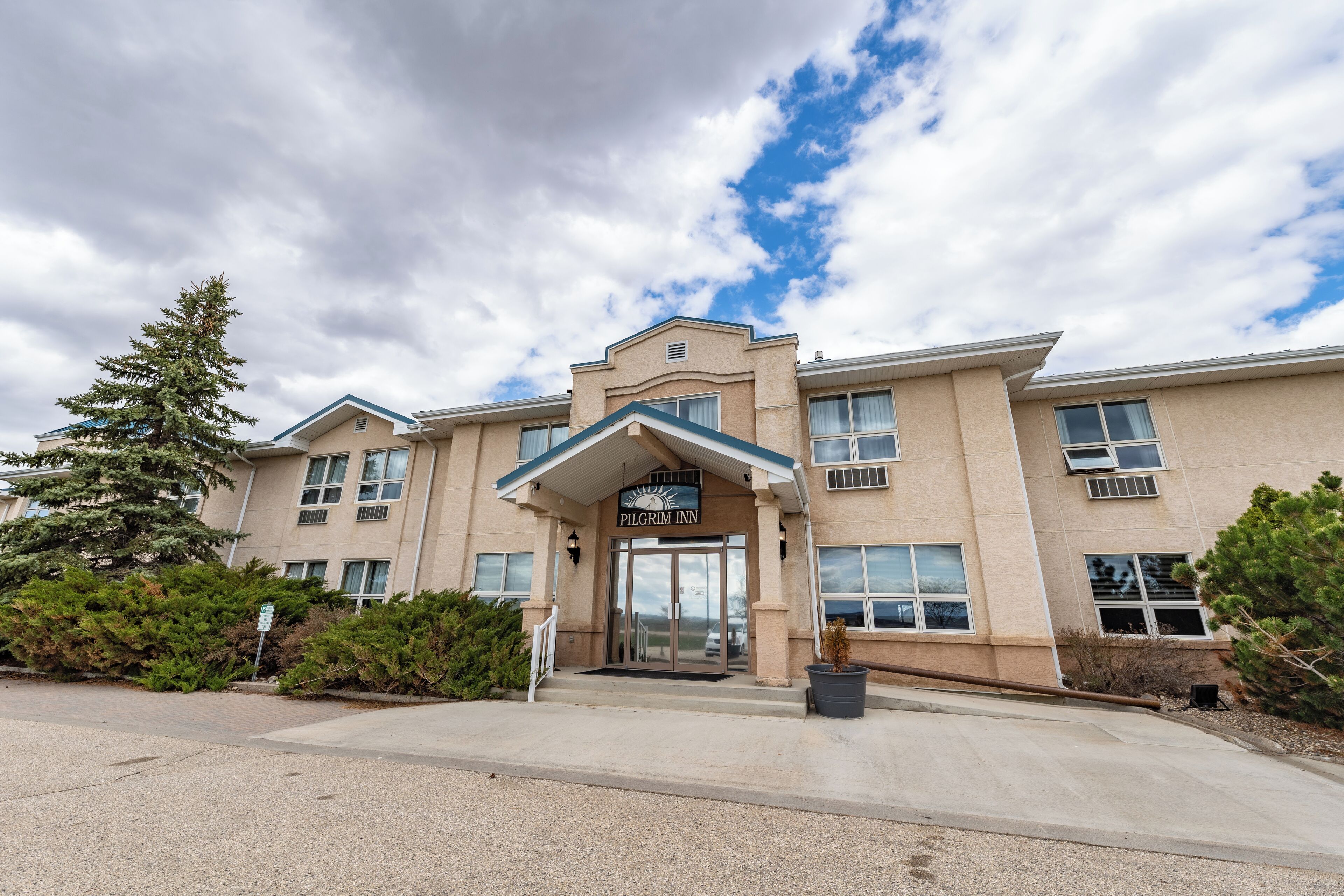 A hotel entrance with a sign reading "PILGRIM INN," a covered entrance, and a parking lot.