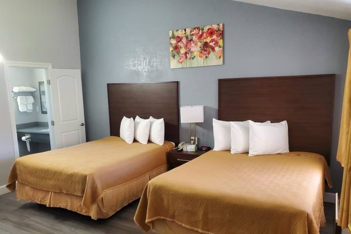 A hotel room with two beds, a painting on the wall, and a bathroom visible through an open door.