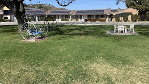 A residential area with solar panels on the roof of a building, a swing set, and a patio with chairs. - Best Way Inn (Paso Robles)