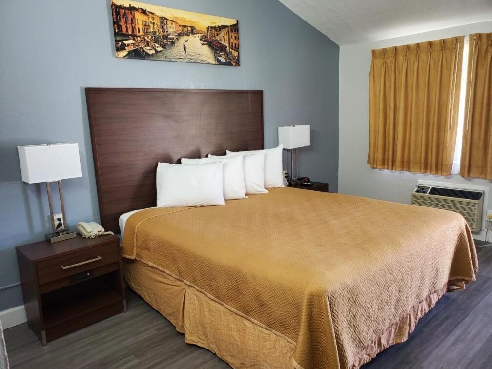 Une chambre d’hôtel avec un grand lit, deux tables de chevet, une commode, un tableau au mur et une fenêtre avec des rideaux.