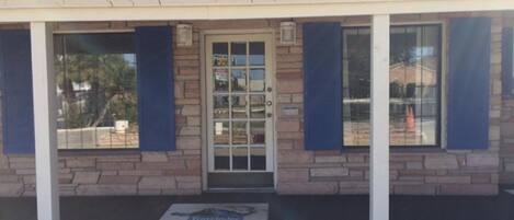 Un edificio con fachada de piedra, una puerta central con paneles de vidrio y contraventanas azules en las ventanas.