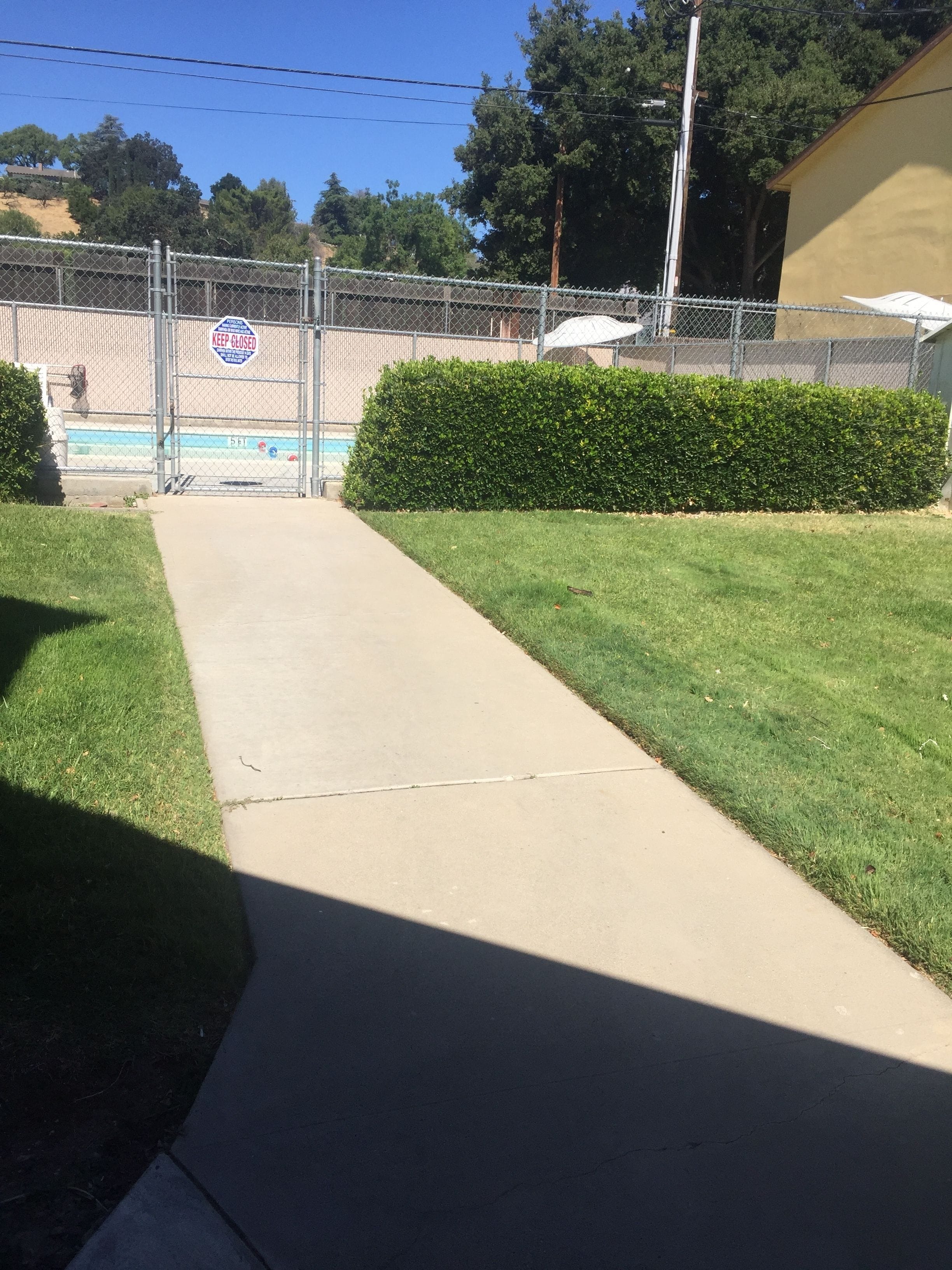 A gated entrance with a 'KEEP CLOSED' sign, a concrete pathway, and a well-maintained hedge.