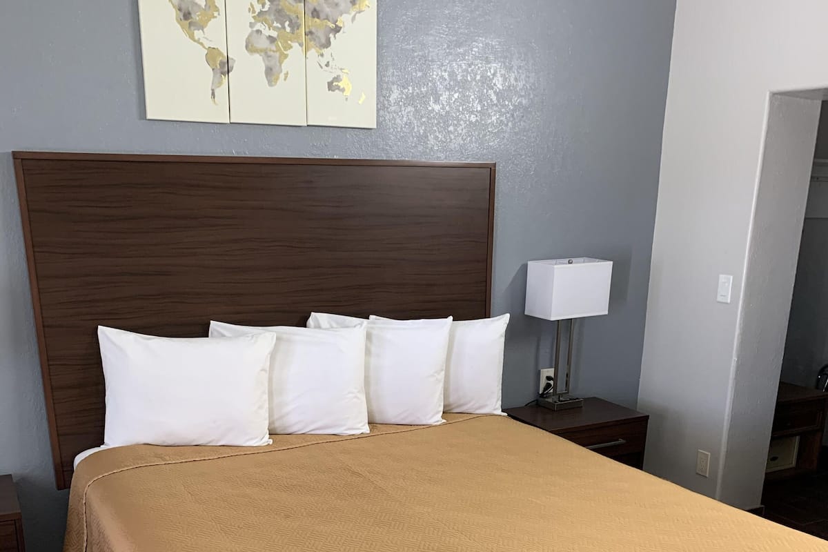 A neatly made bed with a beige bedspread and white pillows, a wooden headboard, a nightstand with a lamp, and a wall-mounted map.