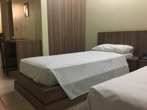 A hotel room with two beds, a wooden headboard, a bedside table with a phone, and a door with a mirror. - Cabiúna Palace Hotel