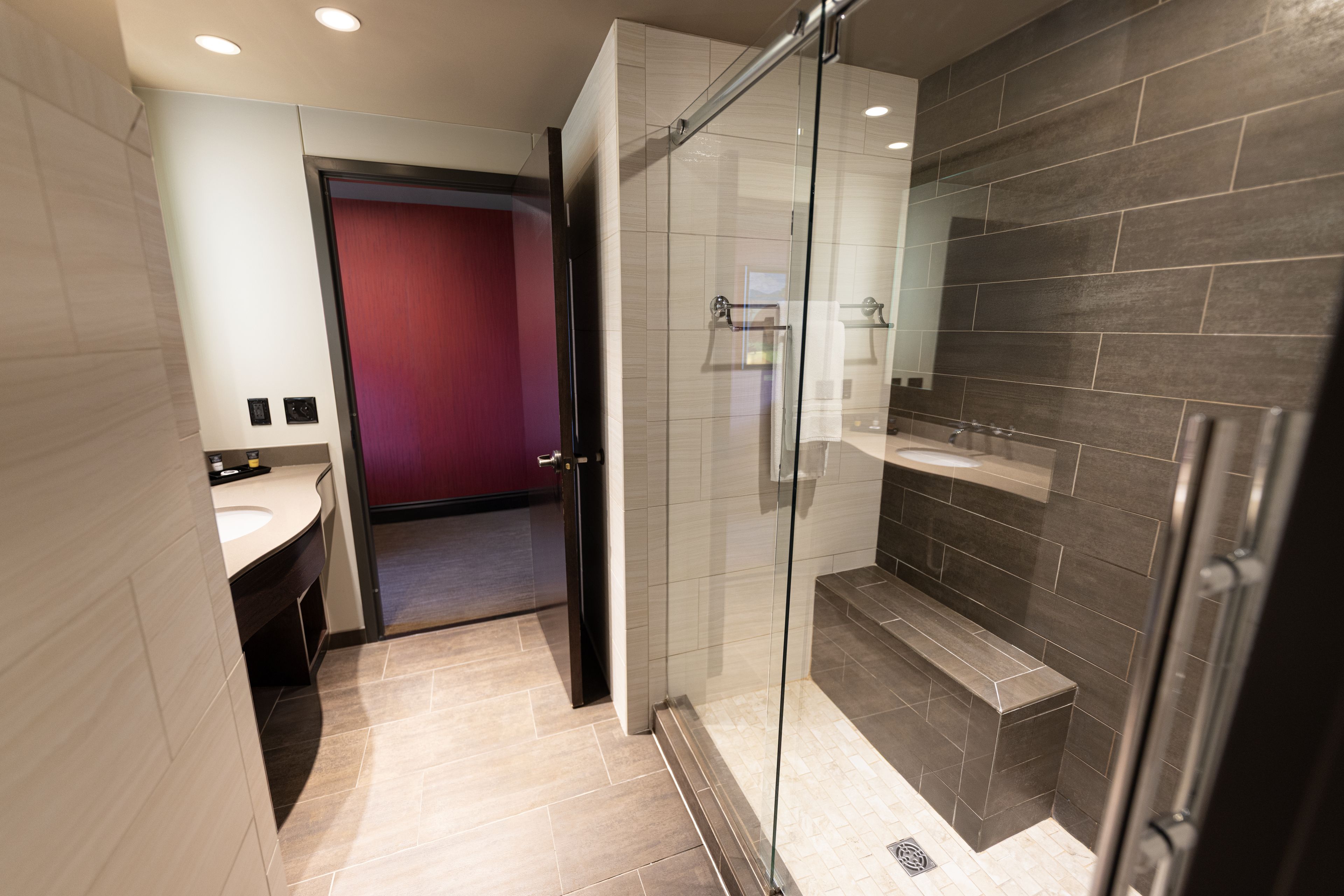 Une salle de bain moderne avec une douche à parois de verre, un meuble-lavabo et un mur d’accent rouge.