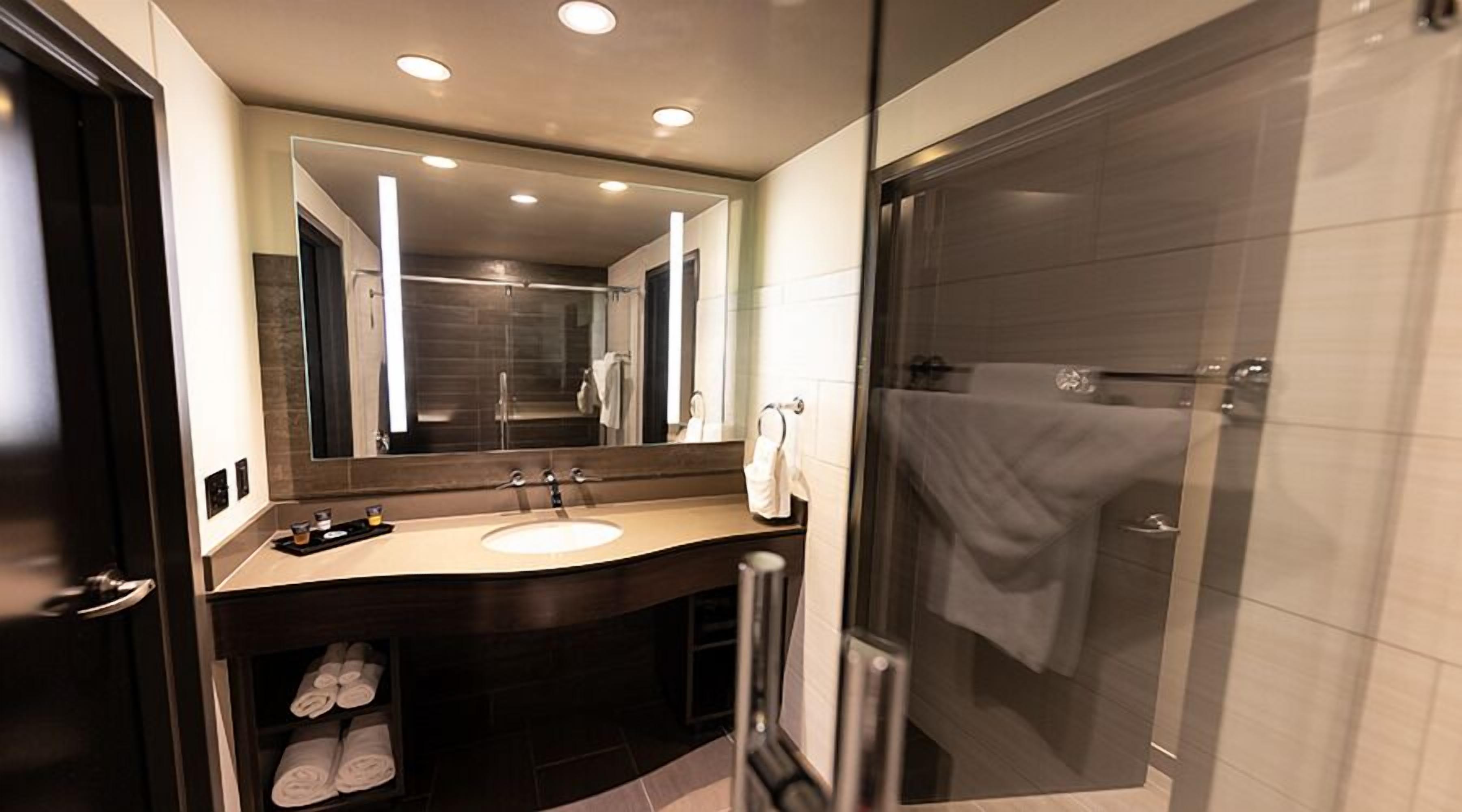 A modern bathroom with a large mirror, a sink, and a shower.