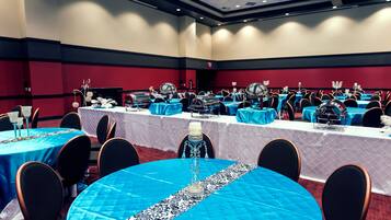 Un salón de conferencias con varias mesas, cada una cubierta con un mantel azul y caminos de mesa blancos. La sala tiene paredes rojas y un techo alto con iluminación empotrada.