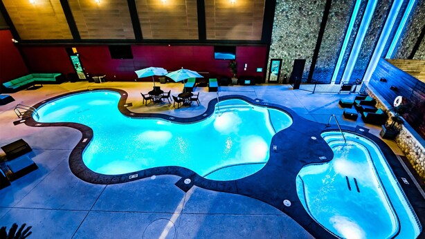 Une piscine intérieure au design ondulé original, entourée de chaises longues et de parasols.