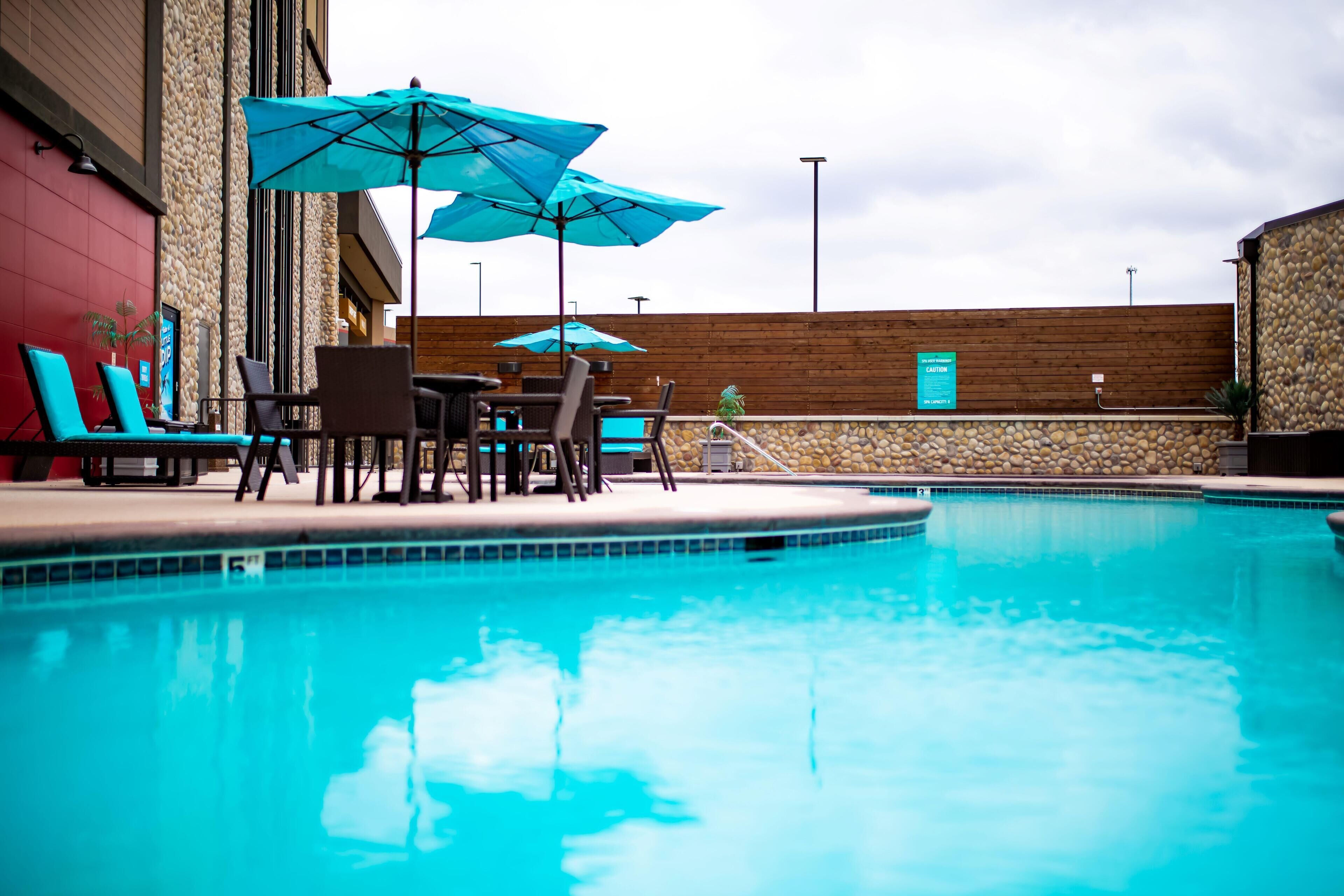 A swimming pool with lounge chairs and umbrellas, surrounded by stone walls and wooden paneling.