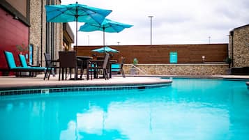 A swimming pool with lounge chairs and umbrellas, surrounded by stone walls and wooden paneling.