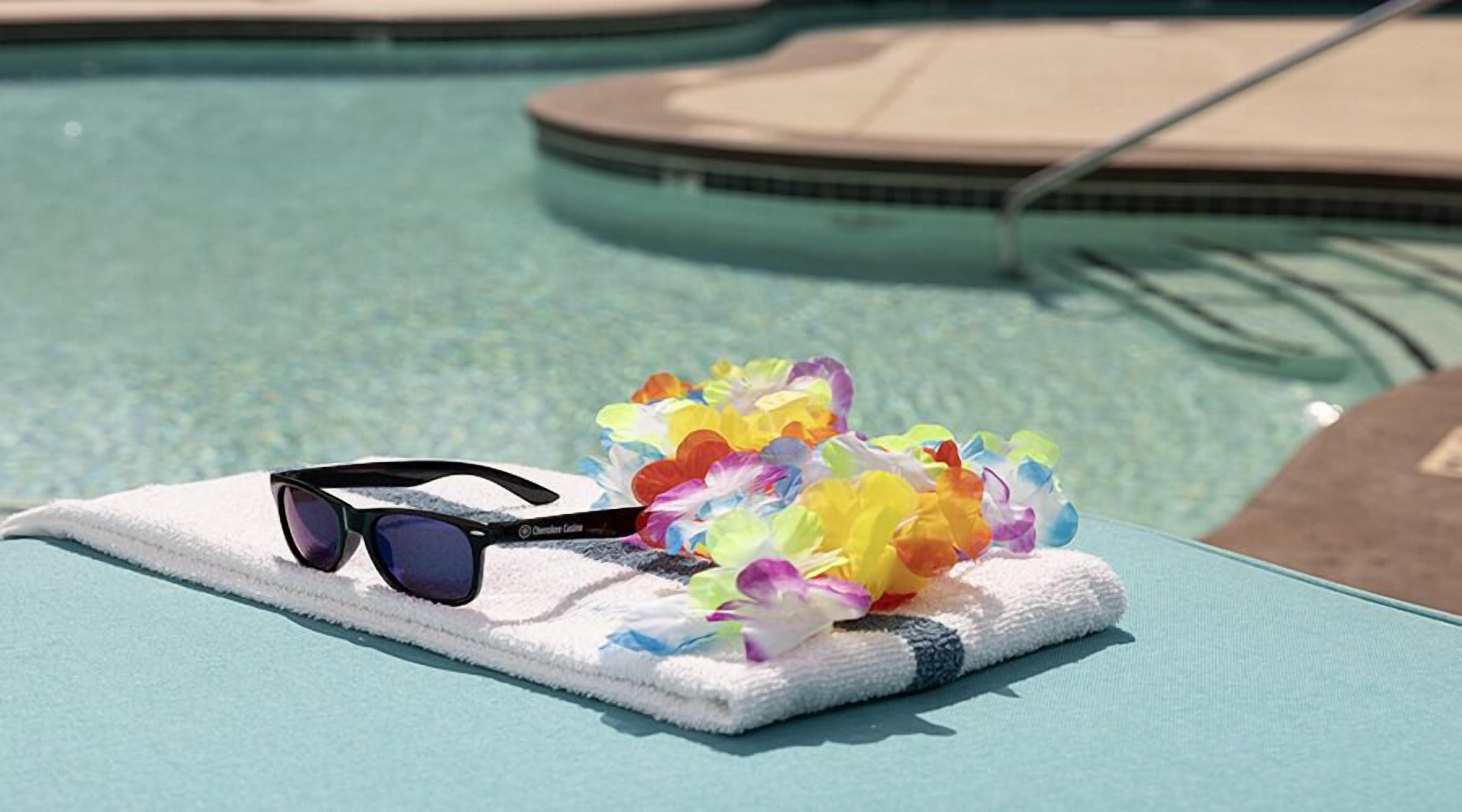 Sunglasses and a lei on a towel by a pool.