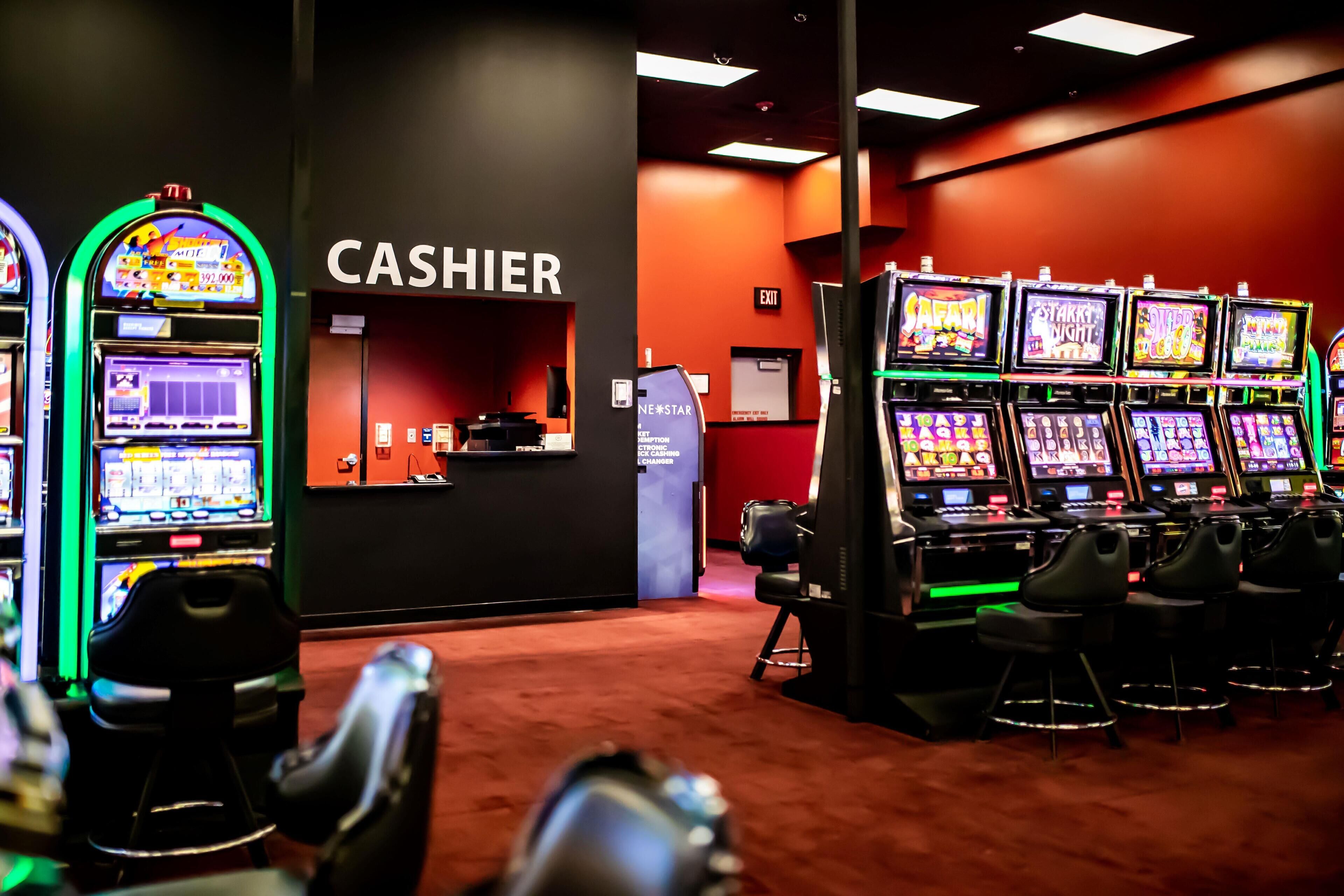 Un casino con múltiples máquinas tragamonedas, una zona de caja y un suelo cubierto de alfombra roja.