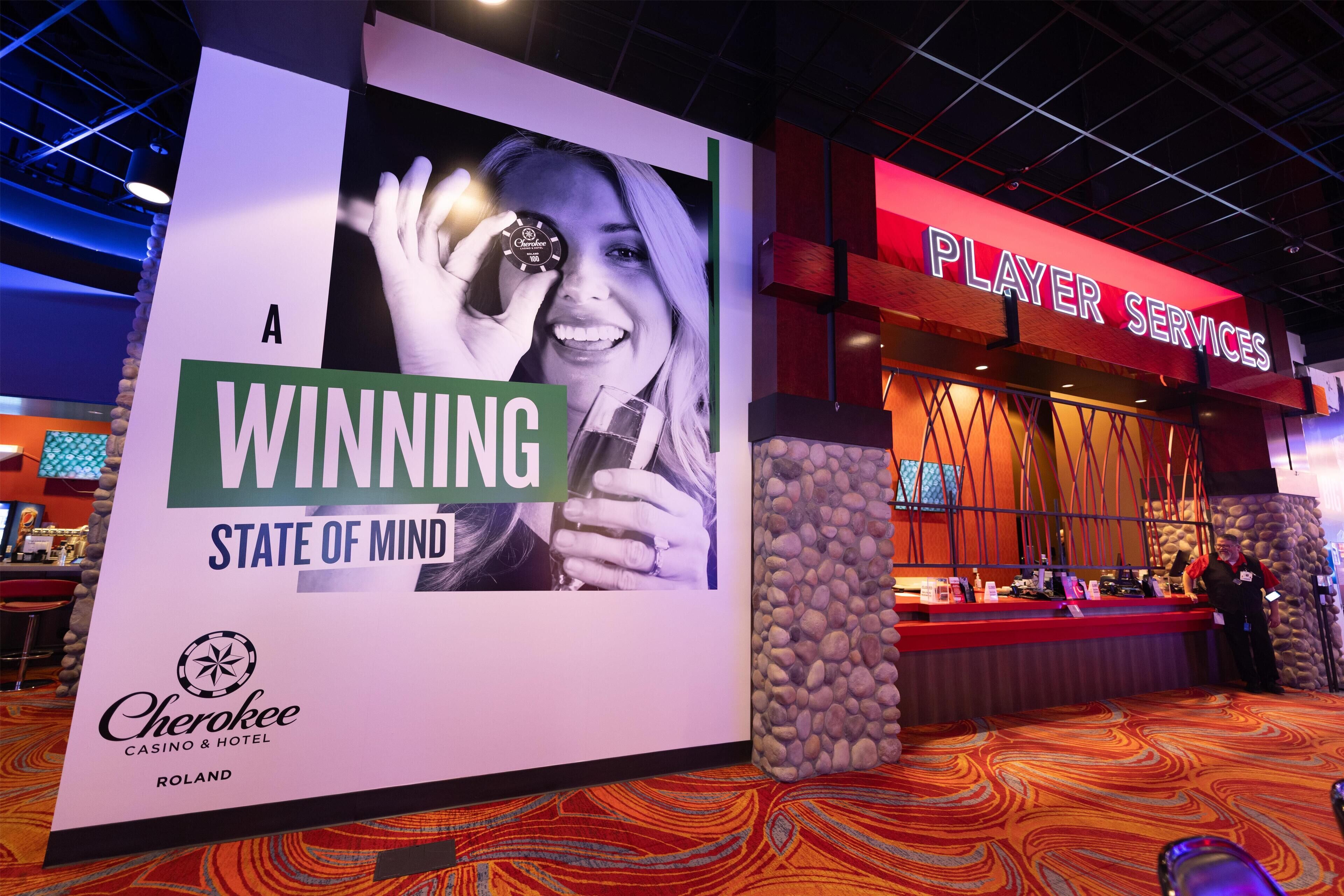 A casino interior with a large promotional sign, a reception area, and a 'Player Services' sign.