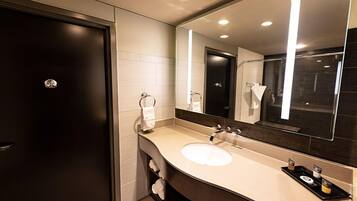 Un baño moderno con una puerta oscura, un lavabo blanco, un espejo grande y una bandeja con artículos de aseo.