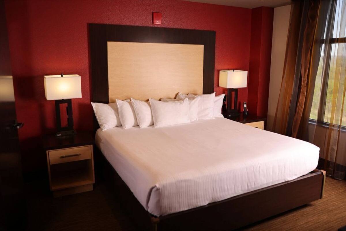 A hotel room with a large bed, two bedside tables with lamps, a wooden headboard, and a red wall.
