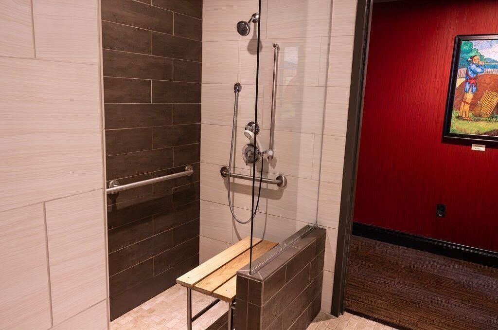 Un espace douche équipé d’un banc en bois, d’une barre d’appui et d’un mur carrelé.