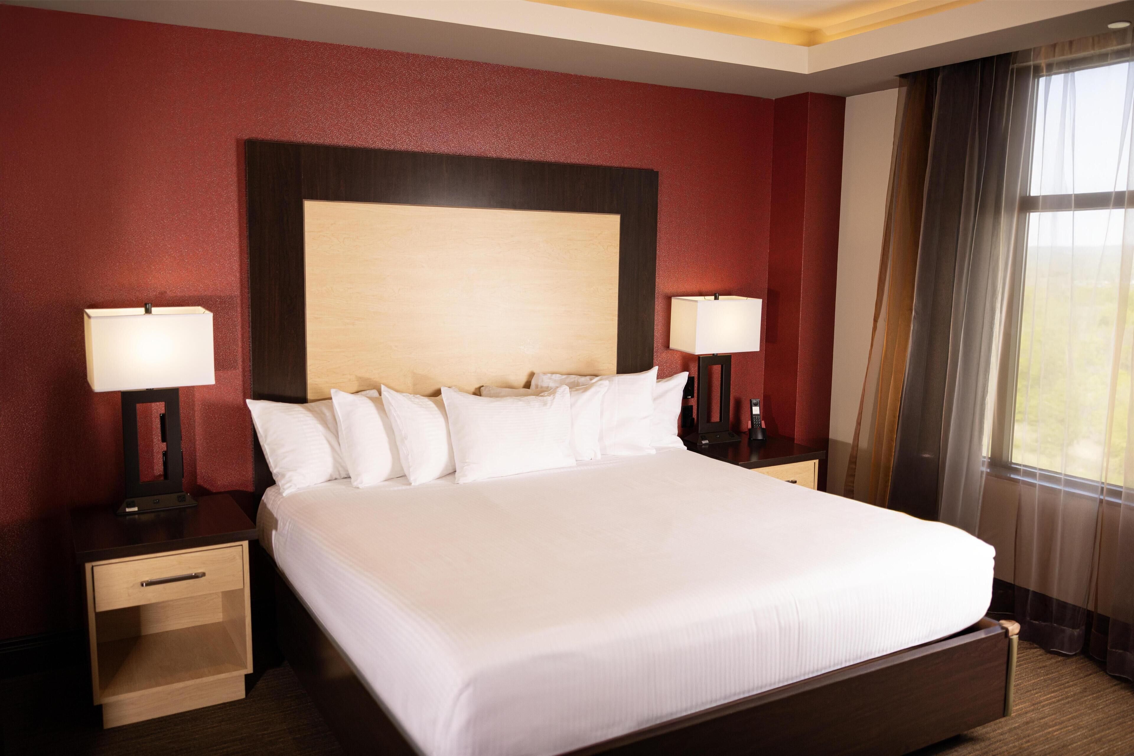 A large bed with white linens, two bedside tables with lamps, and a wooden headboard.