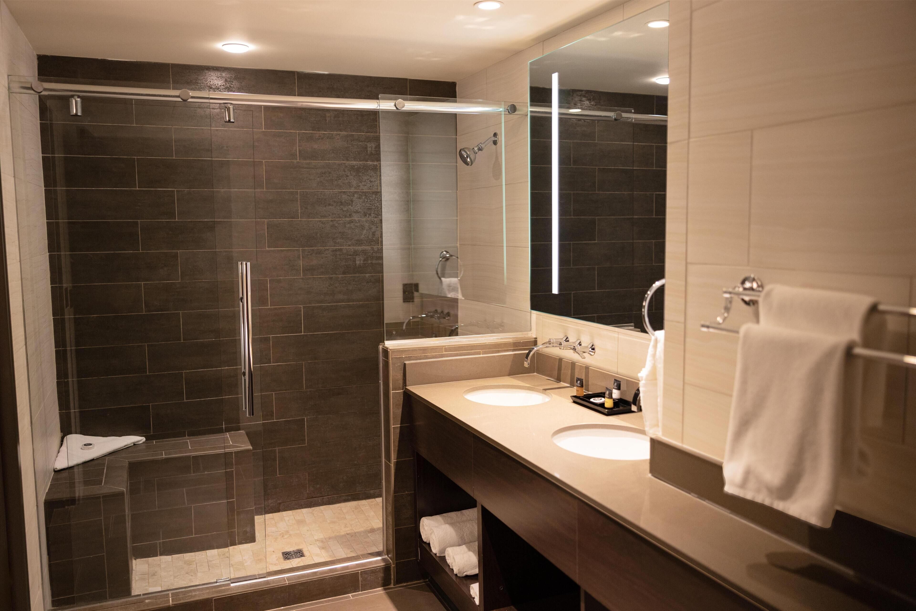 A modern bathroom with a glass-enclosed shower, two sinks, and a large mirror.