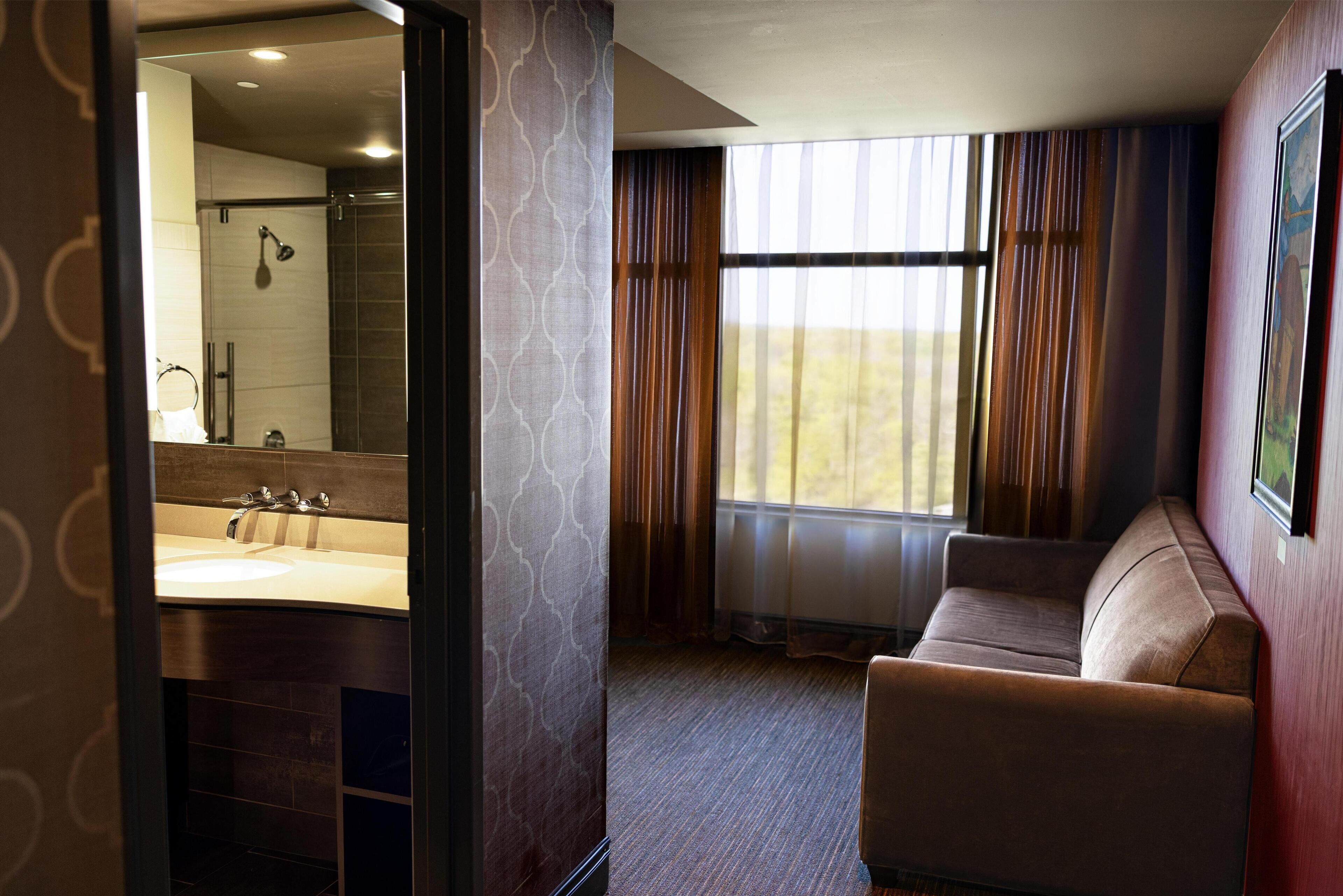 Une salle de bain d’hôtel dotée d’un grand miroir, de deux lavabos, d’une douche et d’un coin salon offrant une vue sur l’extérieur.