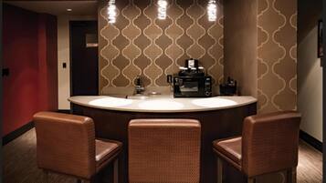Une salle de bain d’hôtel avec un lavabo rond, trois chaises marron et un four à micro-ondes posé sur le comptoir.