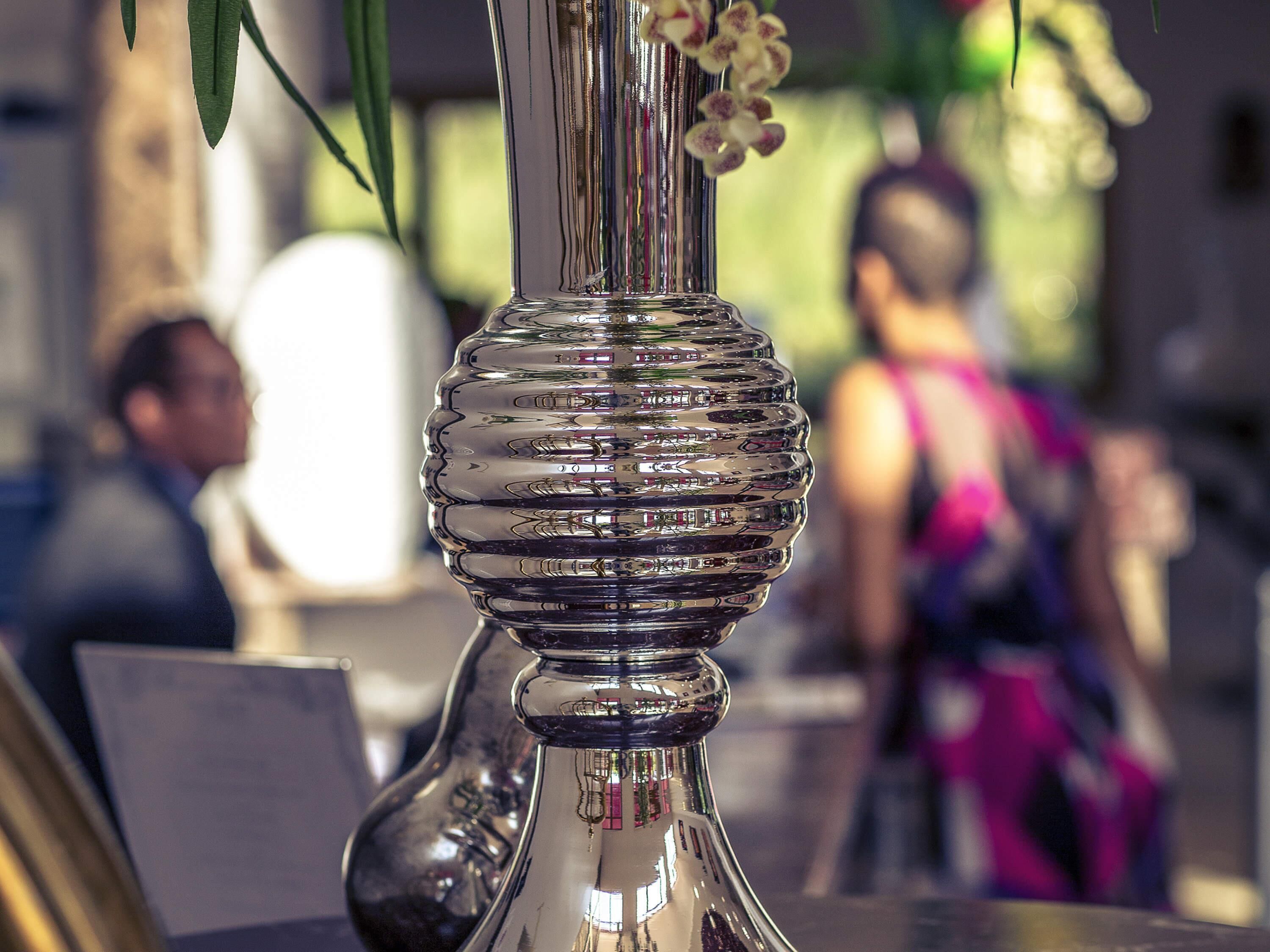 A metallic vase with a reflective surface and a floral arrangement.
