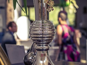 A metallic vase with a reflective surface and a floral arrangement. - Mercure Cayenne Royal Amazonia Hotel (Cayenne)