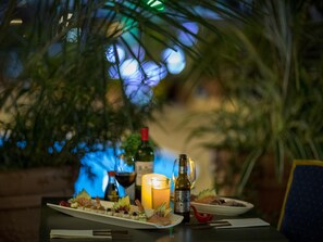 A table set with a variety of appetizers, a candle, and bottles of wine, surrounded by greenery. - Mercure Cayenne Royal Amazonia Hotel (Cayenne)